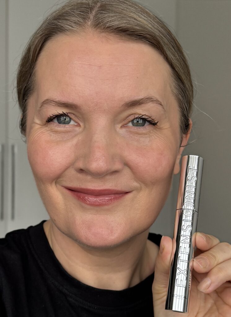 Holding L'Oreal Paris Telescopic Extensionist Mascara showing it applied on both eyes